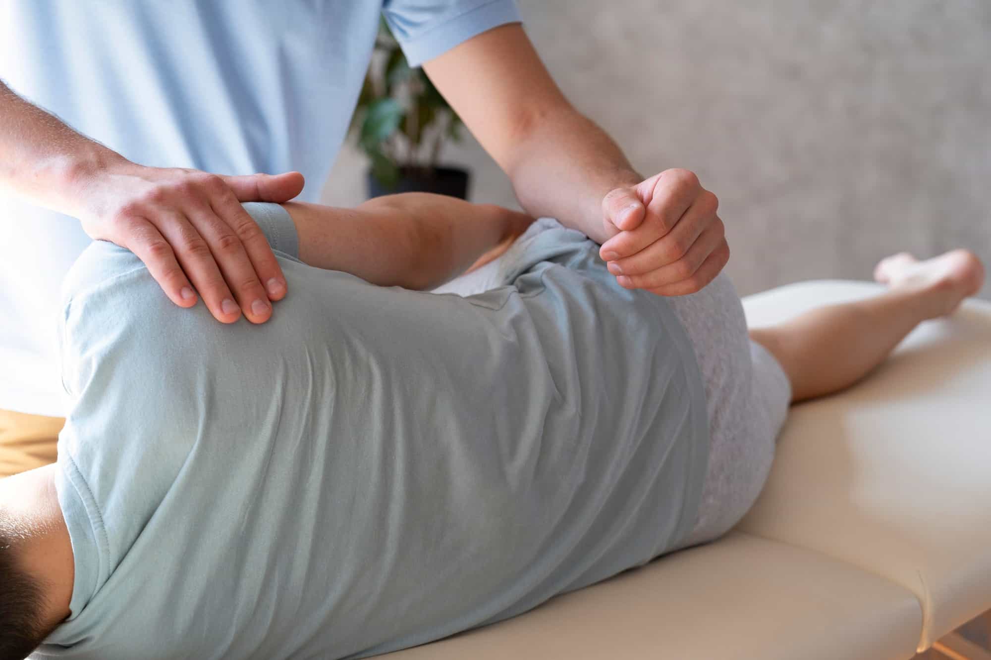 Person, die von einem Therapeuten eine Rückenbehandlung erhält und auf der Seite auf einem Massagetisch liegt.